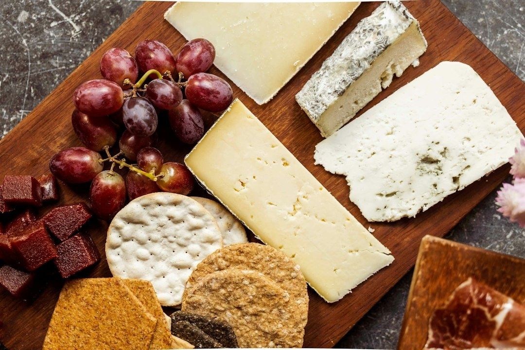 Wooden board with cheeses, red grapes, crackers, and fruit paste